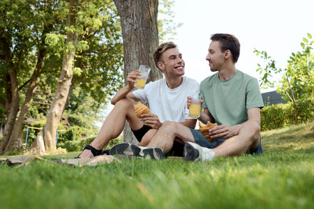 A dapper couple enjoys refreshing drinks and smiles while sitting on the grass.の写真素材
