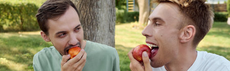 A joyful couple shares a lighthearted moment, savoring apples together outdoors.の写真素材