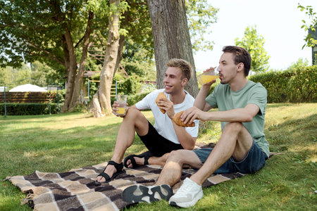 Two joyful friends relax on a blanket, sipping refreshing drinks and sharing moments together.の写真素材
