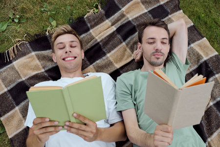 Two men relax on a blanket, deeply engaged in their books while enjoying natures tranquility.の写真素材