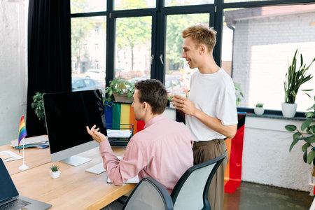 A charming gay couple shares laughter and ideas while working together in a lively office.の写真素材