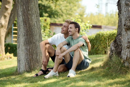 A handsome gay couple relaxes on the grass, sharing laughter and enjoying each others company.の写真素材