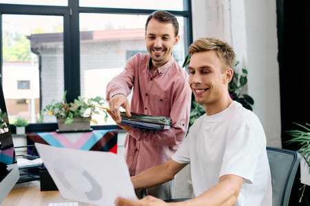 Two happy men share a lighthearted discussion while reviewing creative work together.の写真素材