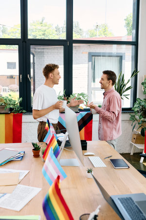 Two smiling individuals enjoy a heartfelt conversation adorned with pride flags in a sunny office.の写真素材