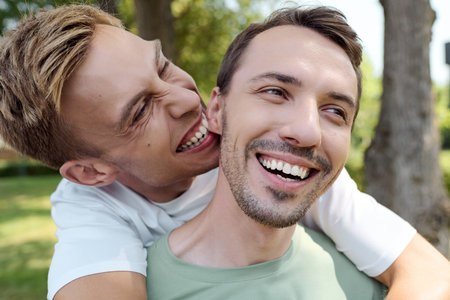 A cheerful couple embraces playfully under the warm sun in a lush park setting.の写真素材
