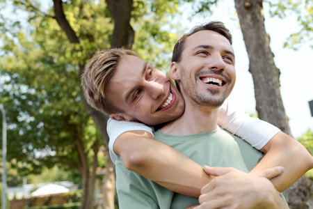 Two happy individuals embrace warmly under the bright sun among lush greenery.の写真素材