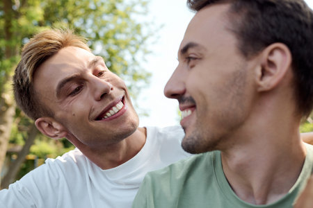 Two charming men share smiles and laughter while embracing in a vibrant park setting.の写真素材