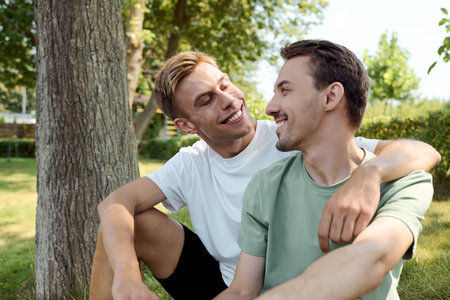 Two charming men share a loving gaze in a sunny park, enjoying each others company.の写真素材