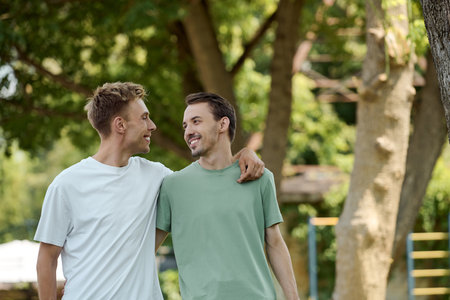 Two friends share a joyful moment walking closely while smiling under the warm sun.の写真素材