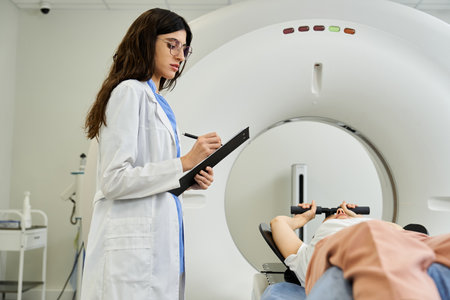 A doctor in a lab coat monitors a patient undergoing an MRI scan in a hospital room.の写真素材