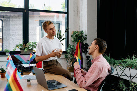 Two men engaged in a lively conversation surrounded by vibrant decorations celebrating pride.の写真素材