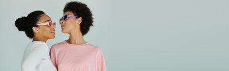 Two young women exchange playful glances while wearing trendy sunglasses, radiating confidence.の写真素材