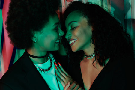 Two friends share a joyful moment, their faces illuminated by colorful lights, radiating happiness.