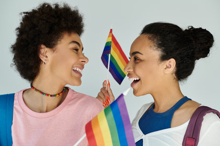 Two cheerful friends smile at each other while waving rainbow flags, celebrating their bond.の写真素材