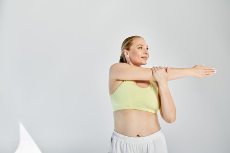 A fit woman in a crop top stretches her arms in a vibrant studio, showcasing her commitment to...