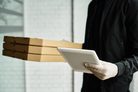 A delivery man wearing gloves brings packages into an office building, ensuring safety.の写真素材