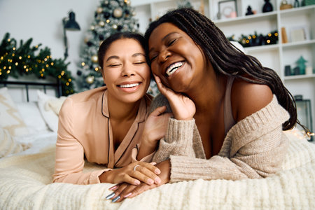 Two women smile warmly while relaxing on a comfortable bed adorned for the holidays.の写真素材