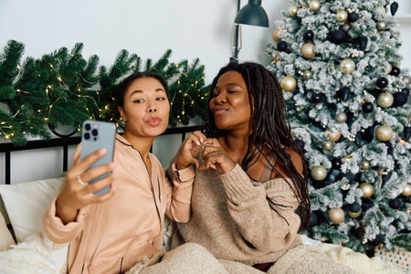 Two women share a tender moment while taking a selfie by a beautifully decorated treeの写真素材