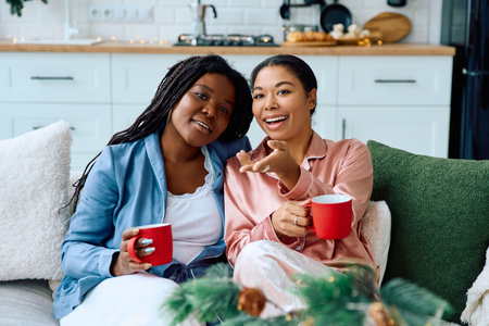 Two women relax on a couch with mugs, sharing laughter and warmth in their stylish space.の写真素材