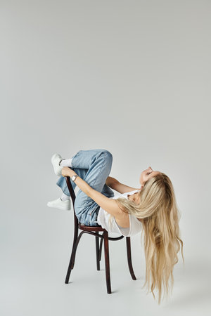 Blonde woman poses creatively on a chair, highlighting modern beauty and fashion trends.の写真素材