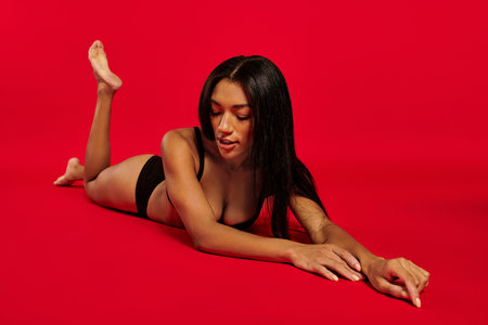 A stunning young Black woman with brunette hair poses in lingerie against a vibrant backdrop.の写真素材