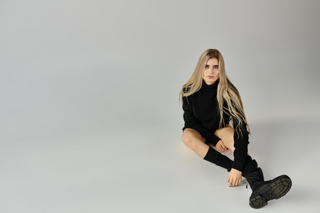 A young woman with long blonde hair poses confidently in stylish black against a sleek backdrop.の写真素材