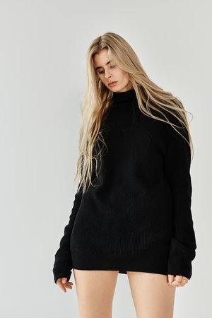Young woman with long blonde hair poses confidently in a minimalist studio environment.