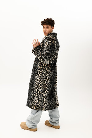 Handsome man strikes a pose in a chic leopard print coat against a clean, bright backdrop.