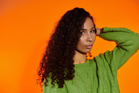 A striking woman in a green sweater and curls captivates with her confident pose.