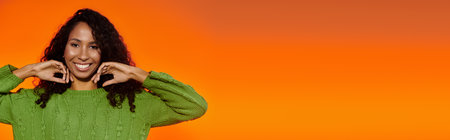 A cheerful woman showcases her joyful personality while posing with an orange backdrop.