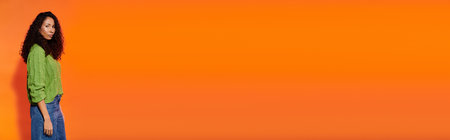 Beautiful woman with curly hair stands confidently in front of an eye catching orange wall.
