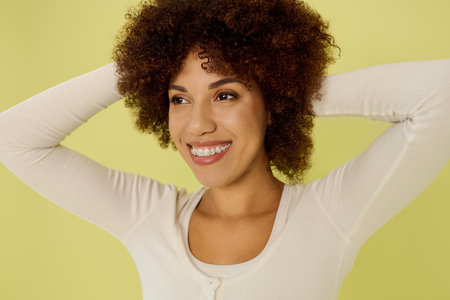 A joyful young woman with curly hair stands confidently in her underwear, radiating positivity on a...