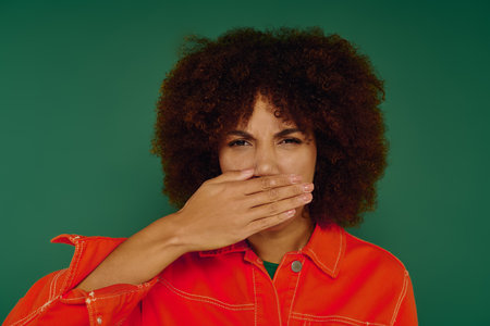 A young woman with curly hair hiding her emotions while dressed casually against a green background.の写真素材