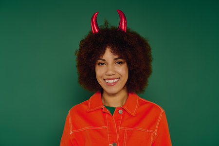 A cheerful young woman with curly hair showcases her playful spirit amidst a bright green backdrop.
