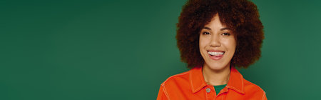 A joyful young African American woman with curly hair smiles in casual wear against a green backdrop.の写真素材