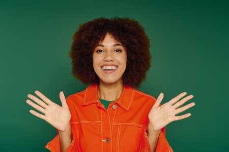 A cheerful young woman with curly hair showcases her joy while wearing casual clothing on a green...