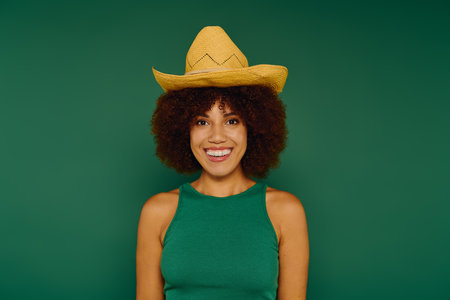 A smiling young African American woman in casual attire shows her lively personality against a green background.の写真素材