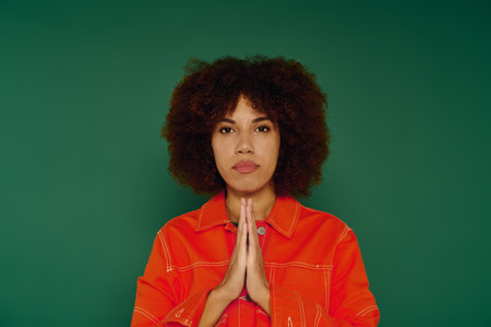 A young African American woman with curly hair conveys strong feelings while standing before a green background.の写真素材
