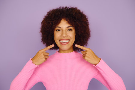 A young African American woman showcases pure happiness and braces, smiling brightly while dressed...