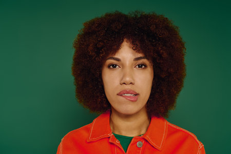 A beautiful young woman with curly hair displays her emotions while wearing casual clothing on a green backdrop.の写真素材