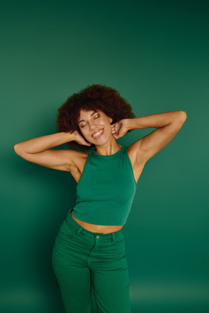 A young woman with curly hair radiates joy, dressed casually in green, enjoying the bright background.の写真素材