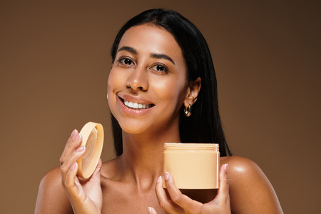 A smiling brunette woman holds a skincare product in a studio, showcasing beauty.