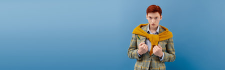 A dapper young man with striking red hair models an elegant winter outfit in a studio setting.
