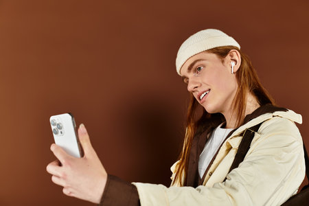 A trendy teenage boy with vibrant red hair poses confidently while capturing a selfie in the studio.の写真素材