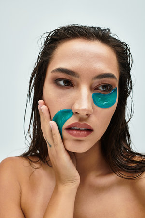 A beautiful woman delicately applies refreshing gel patches to her face, enhancing her glow.の写真素材