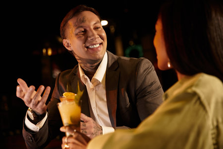 Tattooed young couple shares laughter and drinks during a delightful night out.の写真素材