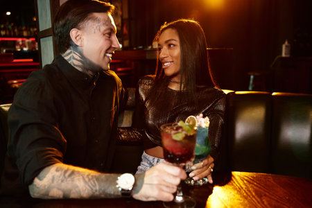 A young couple shares a joyful moment over drinks in a vibrant bar during a night out.の写真素材