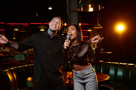 A young couple with tattoos shares a fun moment singing at a lively bar on a night out.の写真素材