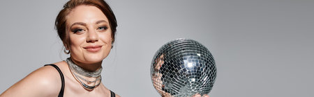 The young woman poses confidently, showcasing her elegance while holding a shimmering disco ball.