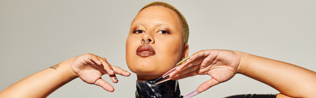 The young woman stands confidently, exuding bold fashion with striking features and unique pose.